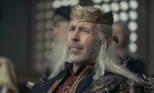 A man wearing a crown sits in a chair surrounded by others.